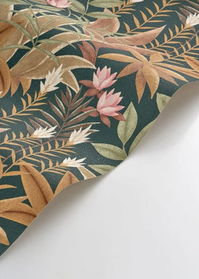 A close-up of a tropical botanical patterned surface, likely wallpaper or fabric, featuring pink flowers and tan leaves on a dark teal-green background, shown folded over on a white surface.